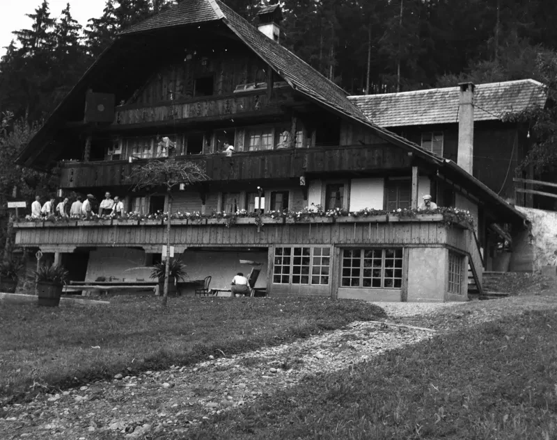 Ein mehrstöckiges Landhaus, auf den Balkonen befinden sich mehrere Personen.