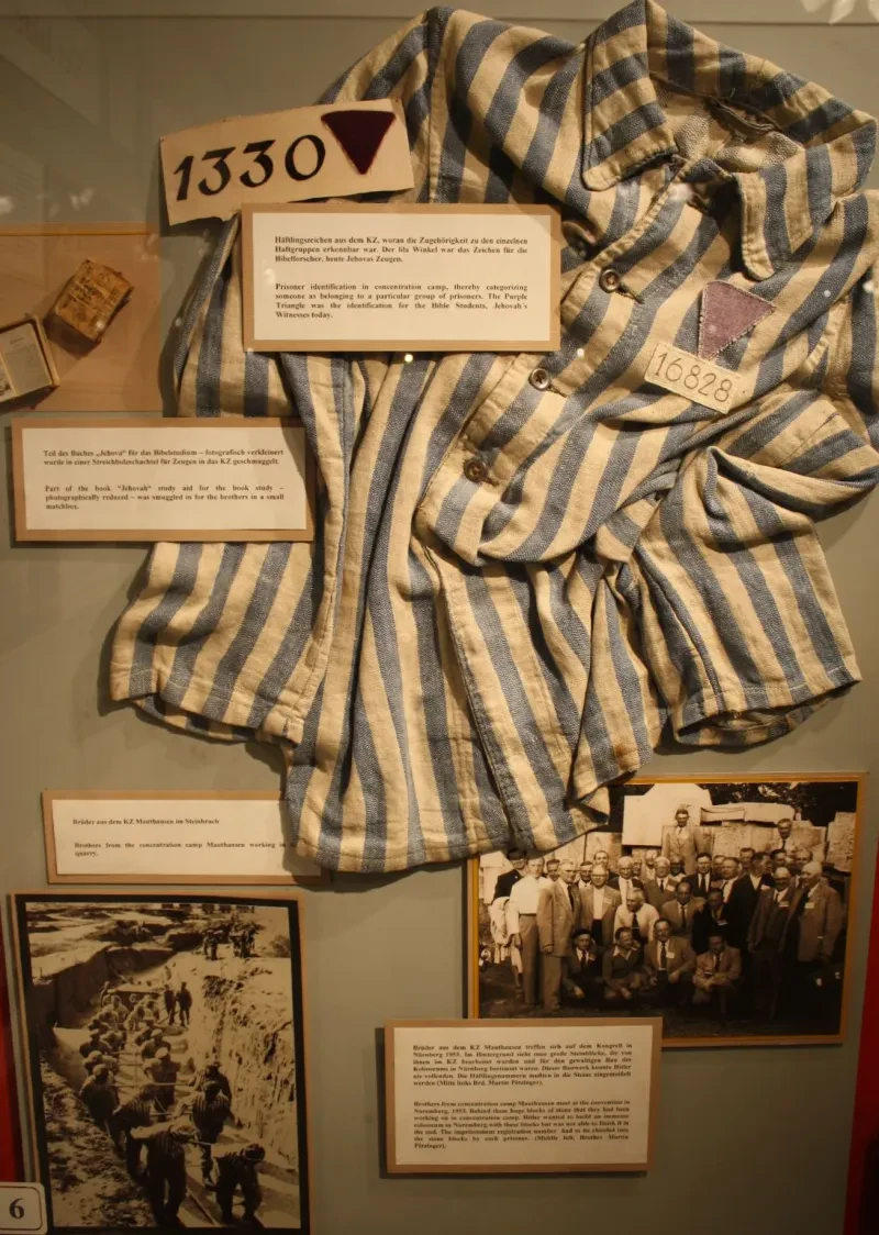 Eine gestreifte Häftlingsjacke vor einem Foto arbeitender Häftlinge im Steinbruch des KZ Mauthausen und einem Foto befreiter Zeugen Jehovas ebenfalls aus dem KZ Mauthausen.