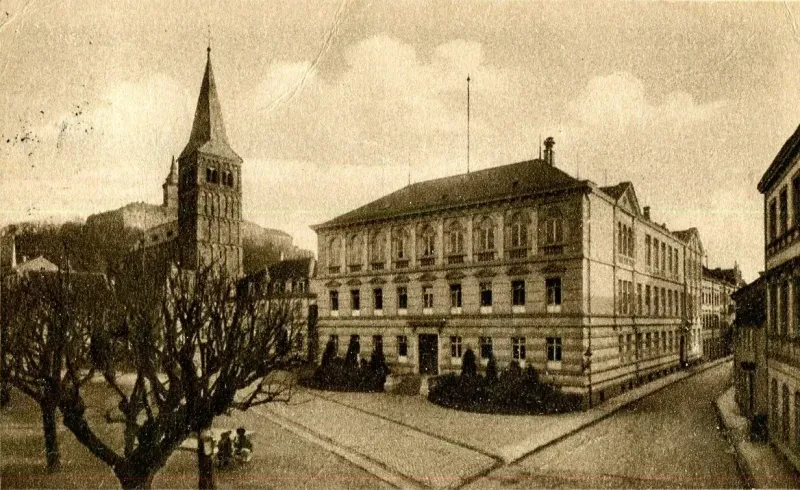 Eine Postkarte zeigt eine Kirche und davor ein dreistöckiges Gebäude.