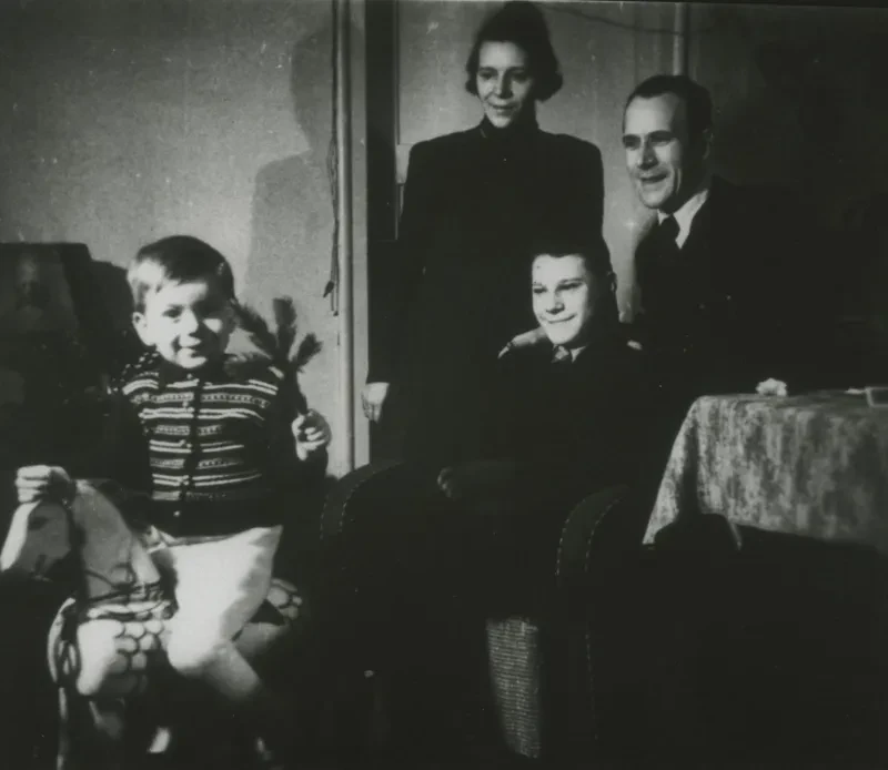 Familienbild: Ein kleiner Junge sitzt auf einem Schaukelpferd, sein großer Bruder in einem Sessel, dahinter stehen Vater und Mutter.