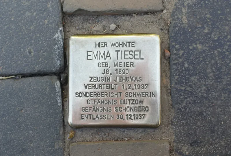 Ein Stolperstein mit der Inschrift: „Hier wohnte Emma Tiesel geb. Meier Jg. 1890 Zeugin Jehovas Verurteilt 1.2.1937 Sondergericht Schwerin Gefängnis Bützow Gefängnis Schönberg Entlassen 30.12.1937“
