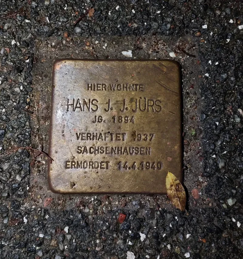 Ein Stolperstein mit der Aufschrift: „Hier wohnte Hans J. J. Jürs / Jg. 1894 / Verhaftet 1937 / Sachsenhausen / Ermordet 14.4.1940“