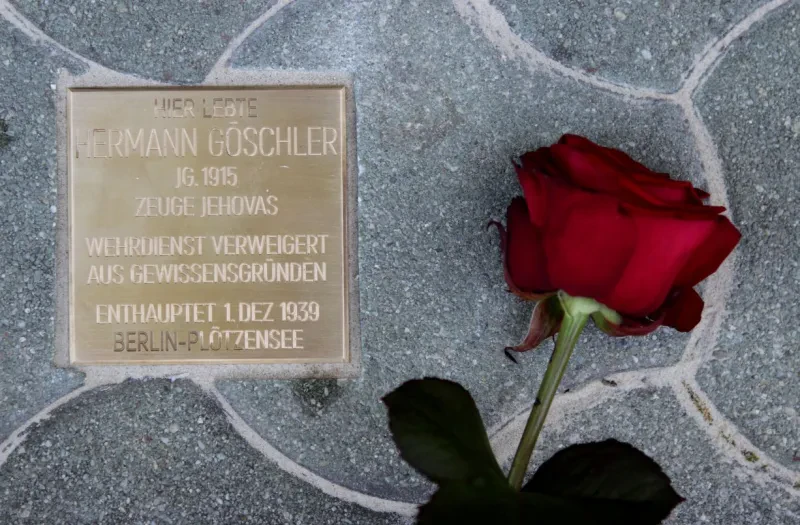 Stolperstein für Hermann Göschler darauf steht eingraviert: Hier lebte Hermann Göschler, Jahrgang 1915 ,Zeuge Jehovas, Wehrdienst verweigert aus Gewissensgründen, enthauptet 1. Dezember 1939 in Berlin-Plötzensee, rechts daneben liegt eine rote Rose am Boden