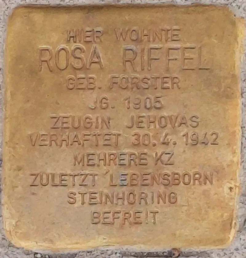 Ein Stolperstein mit der Inschrift: "HIER WOHNTE ROSA RIFFEL GEB. FORSTER JG. 1905 ZEUGIN JEHOVAS VERHAFTET 30.4.1942 MEHRERE KZ ZULETZT 'LEBENSBORN' STEINHÖRING BEFREIT"