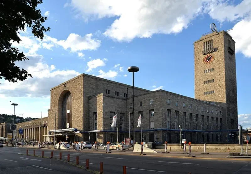Ein graues, vierstöckiges, langestrecktes Gebäude mit hoher Eingangshalle und Uhrenturm.