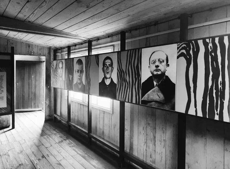 In einer Holzbaracke sind eine Reihe Fotos ehemaliger Häftlinge aufgehängt.
