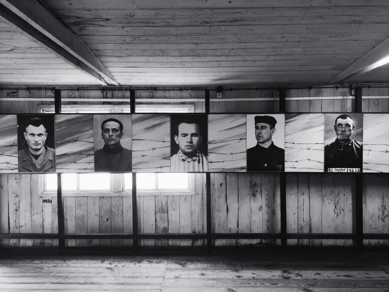 In einer Holzbaracke sind eine Reihe Fotos ehemaliger Häftlinge aufgehängt.