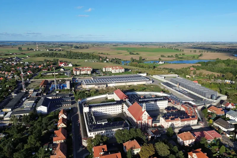 Luftbild mit Blick auf eine Gefängnisanlage. Im Hintergrund das weite Land und blauer Himmel.