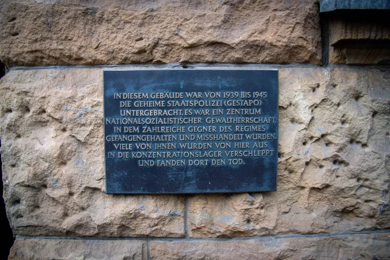 Tefel mit der Aufschrift: »In diesem Gebäude war von 1939 bis 1945 die Geheime Staatspolizei (Gestapo) untergebracht. Es war ein Zentrum nationalsozialistischer Gewaltherrschaft, in dem zahlreiche Gegner des Regimes gefangengehalten und misshandelt wurden. Viele von ihnen wurden von hier aus in die Konzentrationslager verschleppt und fanden dort den Tod.«