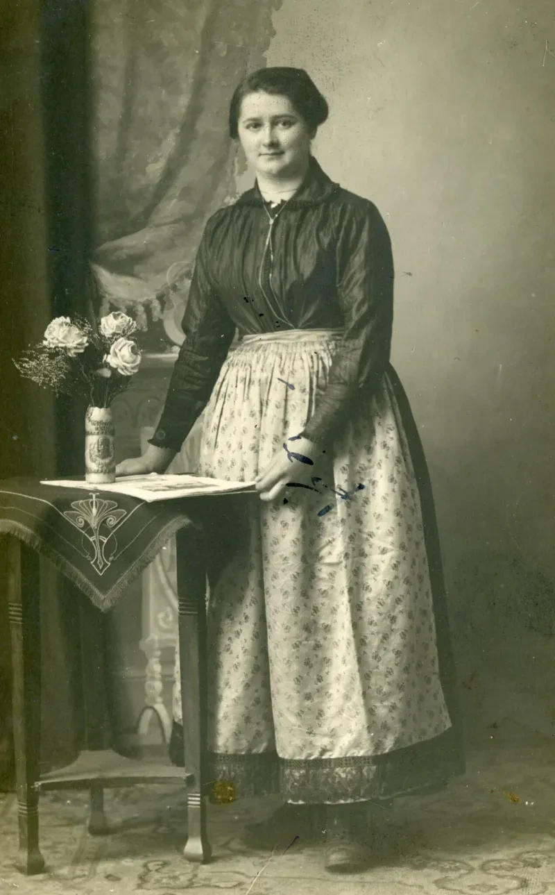 Emma Bauroth, um 1920. Sie steht neben einem Vorhang an einem kleinen Tisch.
