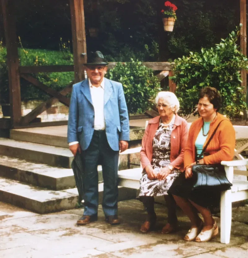 Willy und Emma Thiel (mitte) zu besuch in Thüringen, Mitte der 1970er Jahre. Emma Thiel und eine Glaubensschwester sitzen auf einer Bank in einem Park, Willy Thiel steht links daneben.
