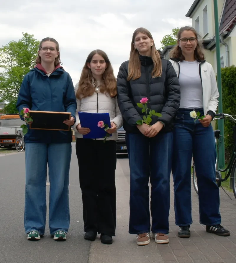 Vier Schülerinnen stehen nebeneinander, sie haben Rosen in den Händen und zwei halten je eine Mappe.