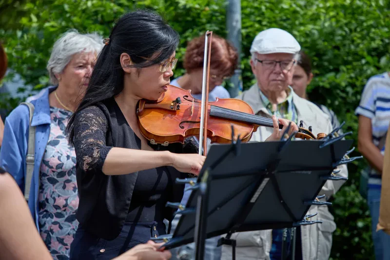 Im Vordergrund eine Violinistin mit Instrument und Notenpult, die spielt.