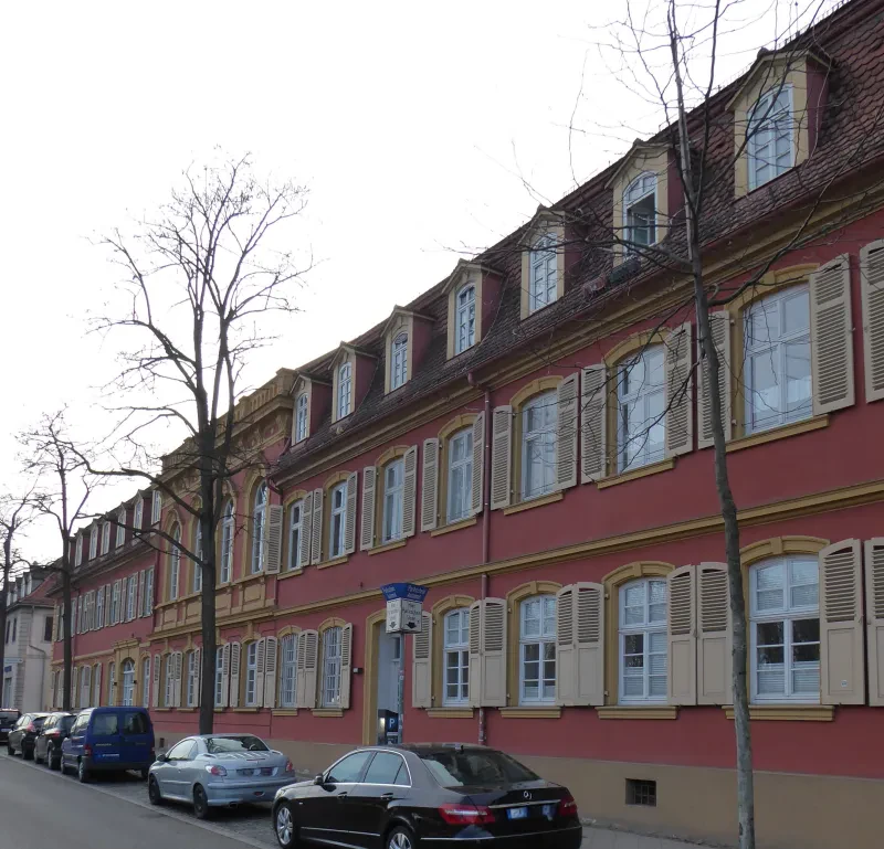 Ein dreistöckiges rot angestrichenes Gebäude mit davor parkenden Autos.
