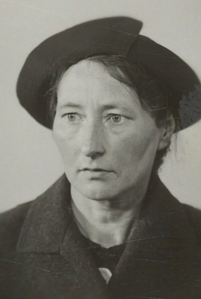 Ein Frau mittleren Alters mit einem schicken Hut und ernstem Blick.