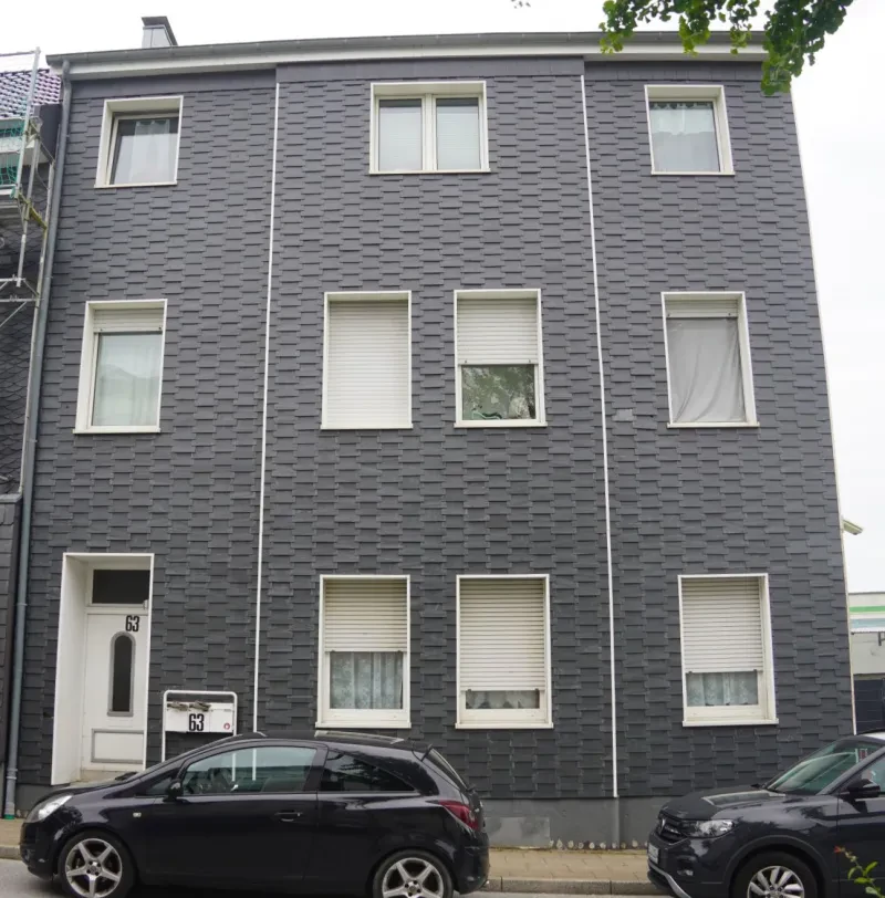 Ein dreistöckiges Wohnhaus mit einer Fassade aus dunklem Bergischen Schiefer. Jede Etage hat zur Straßenseite drei oder vier Fenster.