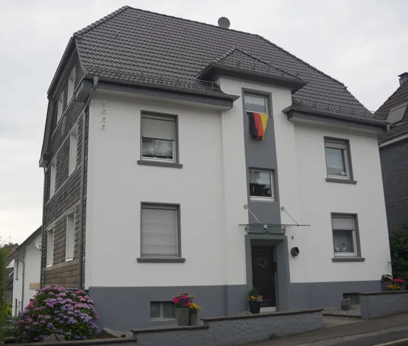 Ein freistehendes dreistöckiges Wohnhaus, dessen Dach und Seitenfassade aus Bergischem Schiefer bestehen.
