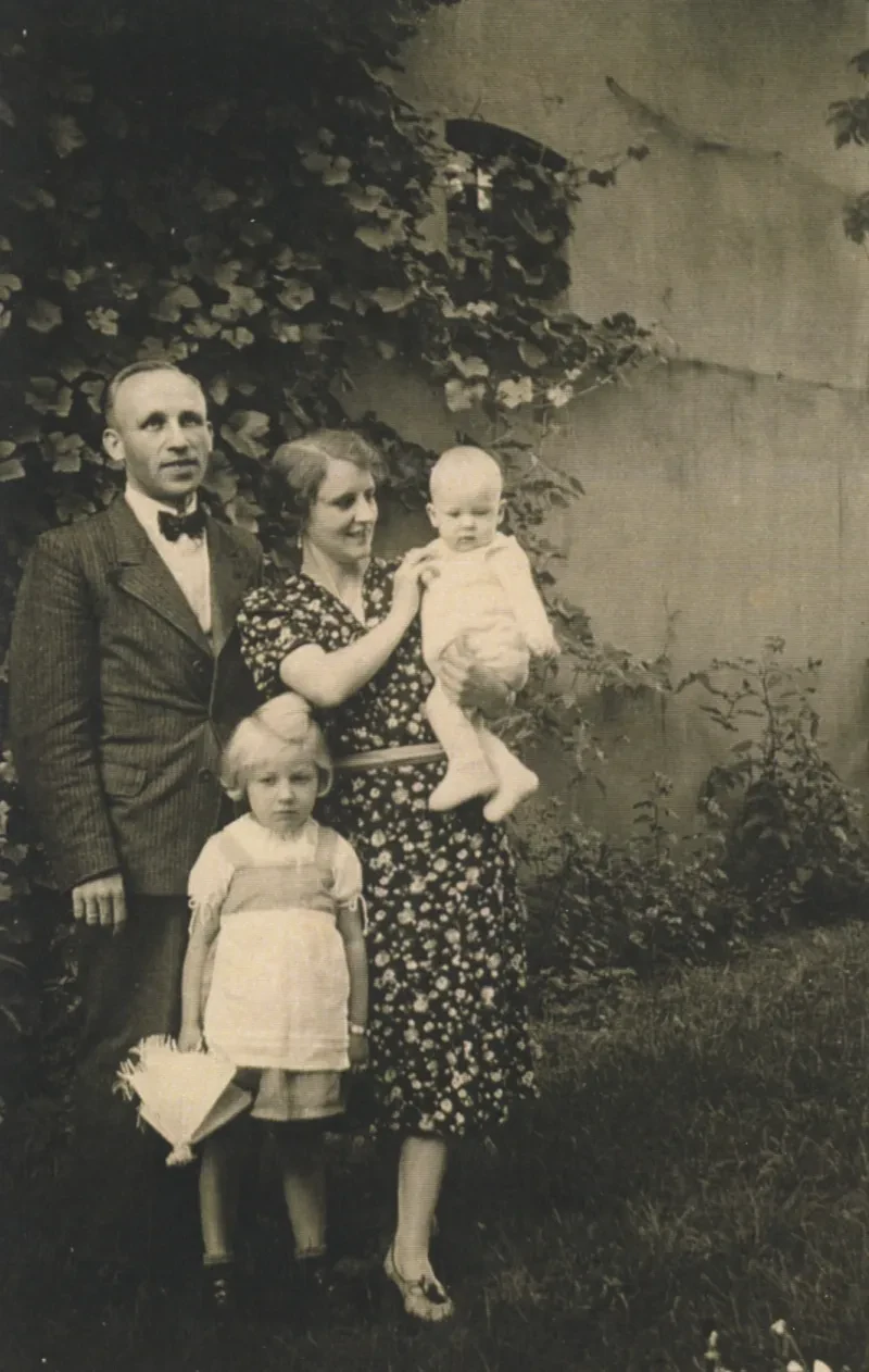 Familienbild: Vater, Mutter und zwei kleine Mädchen vor einer Mauer.
