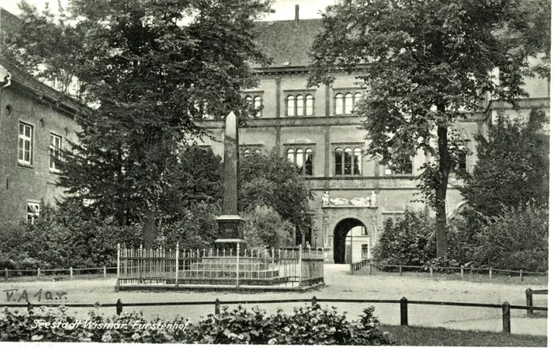 Der Wismarer Fürstenhof, auf dem Platz davor stehen Bäume und ein Obelisk.