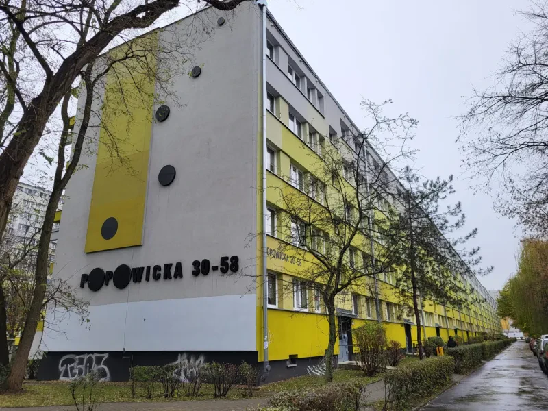 Ein langgestreckter, gelb-weiß gestrichener, fünfstöckiger Wohnblock mit 15 Eingängen.