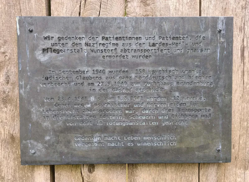 Eine Gedenktafel mit dem Text: "Wir gedenken der Patientinnen und Patienten, die unter dem Naziregime aus der Landes-Heil-und-Pflegeanstalt Wunstorf abtransportiert und grausam ermordet wurden. Im September 1940 wurden 158 psychisch kranke jüdischen Glaubens aus ganz Norddeutschland hierher verbracht und am 27.9.1940 zum Zuchthaus Brandenburg in den Gastod geschickt. Vom 23.41.1941 bis zum 1.8.1941 wurden 212 Kranke, denen wegen psychischer und Nervenleiden ihr Lebensrecht abgesprochen war, durch drei Transporte in die Anstalten Idstein, Scheuern und Eichberg und von dort in Tötungsanstalten gebracht. Gedenken macht Leben menschlich. Vergessen macht es unmenschlich".
