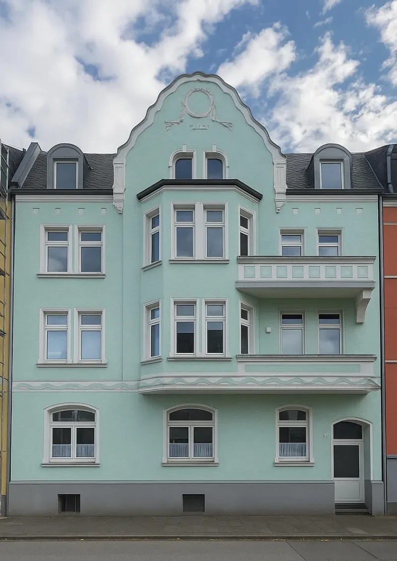Ein vierstöckiges, türkis verputztes Wohnhaus mit ausgebautem Satteldach.