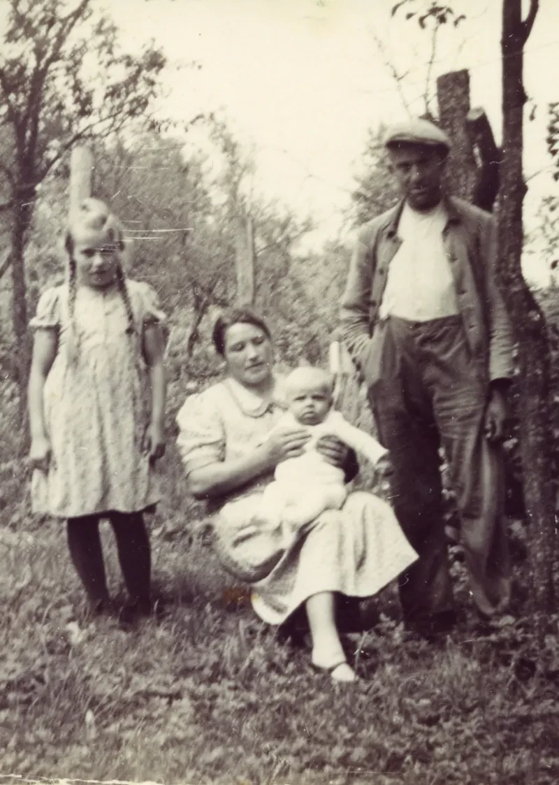 Eine Familie in einem Garten, die Mutter sitzt in der Mitte und hält ein Baby.