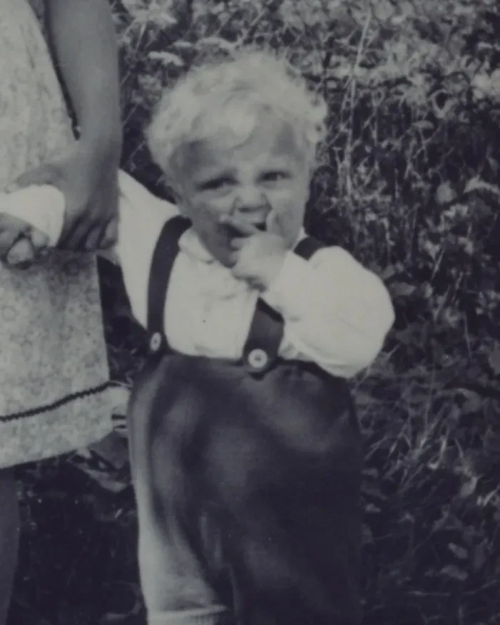 Ein kleiner Junge an der Hand seiner Schwester. Die andere Hand hält er vor dem Mund.
