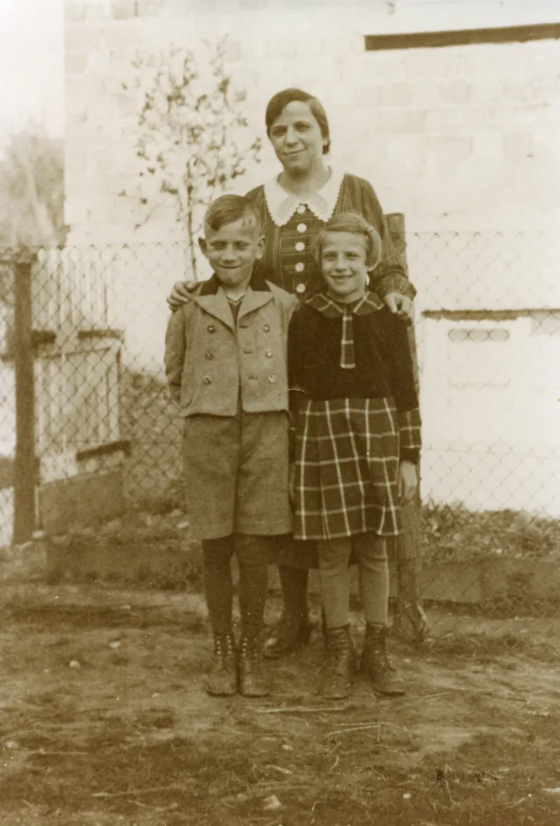 Eine Mutter mit Tochter und Sohn. hinter ihnen ein Drahtzaun.