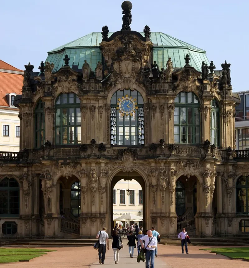 Ein barockes, rundes, zweistöckiges Gebäude mit einem Tordurchgang zur Altstadt. Im lichtdurchflutetem oberen Stockwerk befindet sich ein Fenster mit einem Glockenspiel.